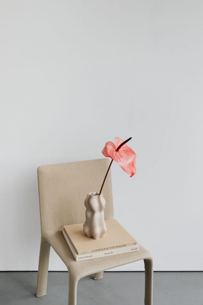 An elegant anthurium flower in a sculptural vase on a minimalist chair.
